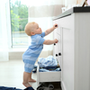 small child wearing a blue onesie reaching for the top drawer of a dresser
