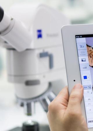 Someone using a tablet to measure distance with a blurred microscope in the background 