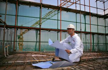 Bureau Veritas employee kneeling on a building under construction holding plans