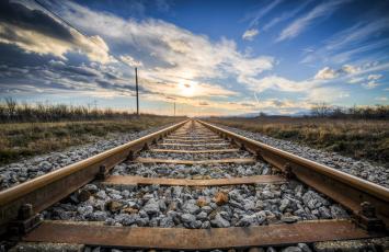 Railroad track with gravel underneath and the sun setting in the distance