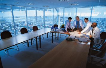 Four businessmen reviewing plans in a conference room overlooking the floor below