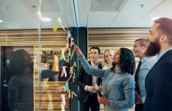 Group of business people reading post it notes on a glass wall